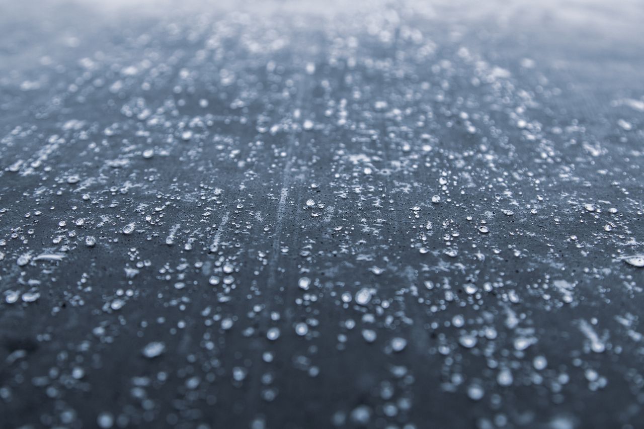 Close-up view of water droplets scattered on a dark textured surface, creating an abstract pattern.