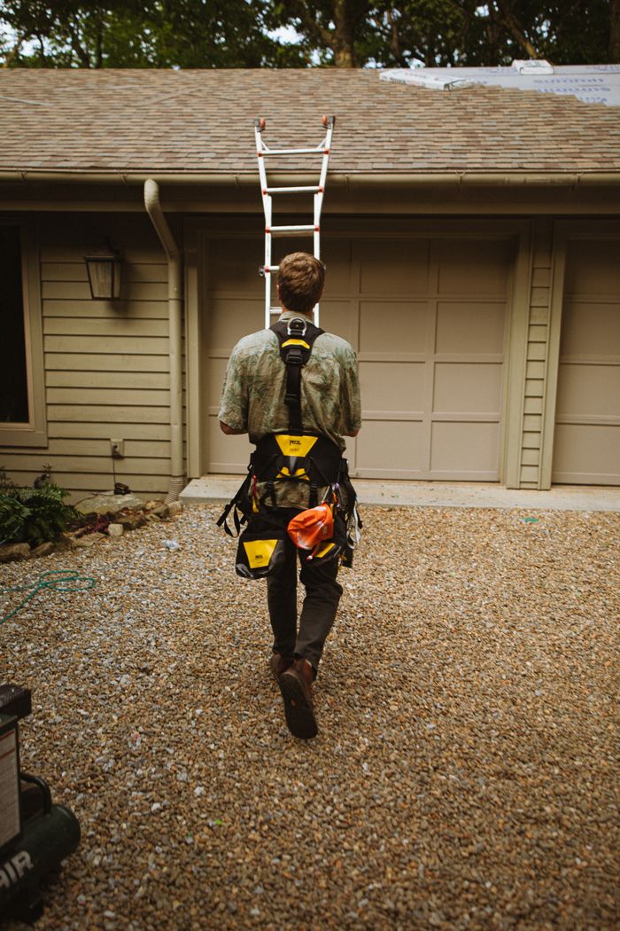 A construction worker climbing a ladder to a roof, using safety gear in North Carolina.